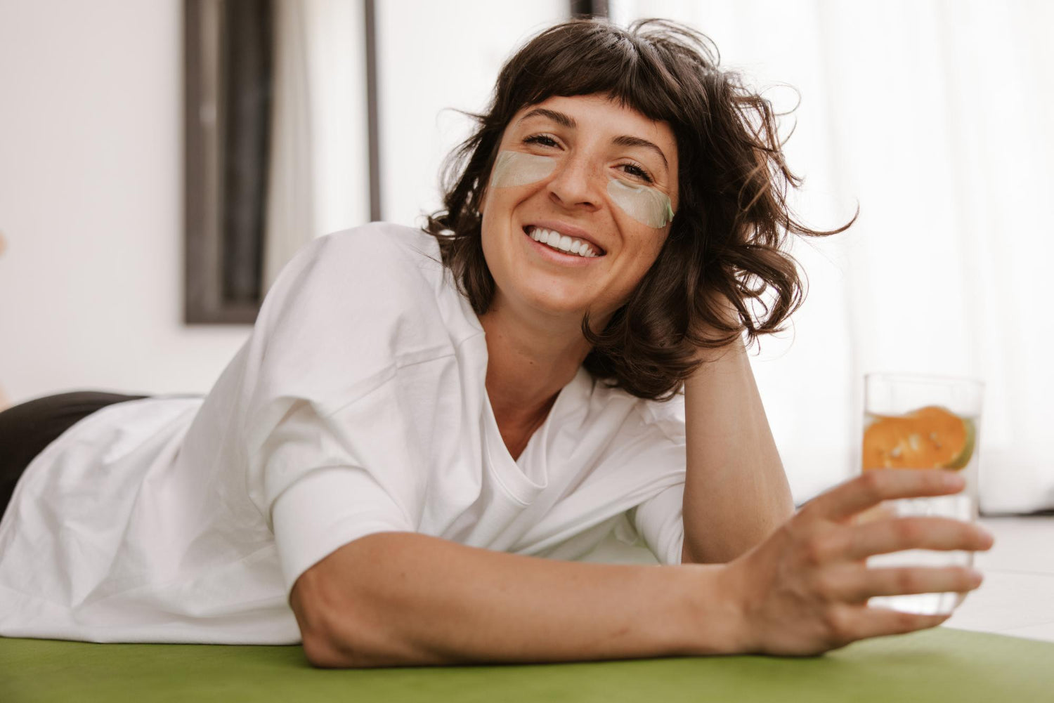 Close up view of smiling woman with patches with glass water look at camera